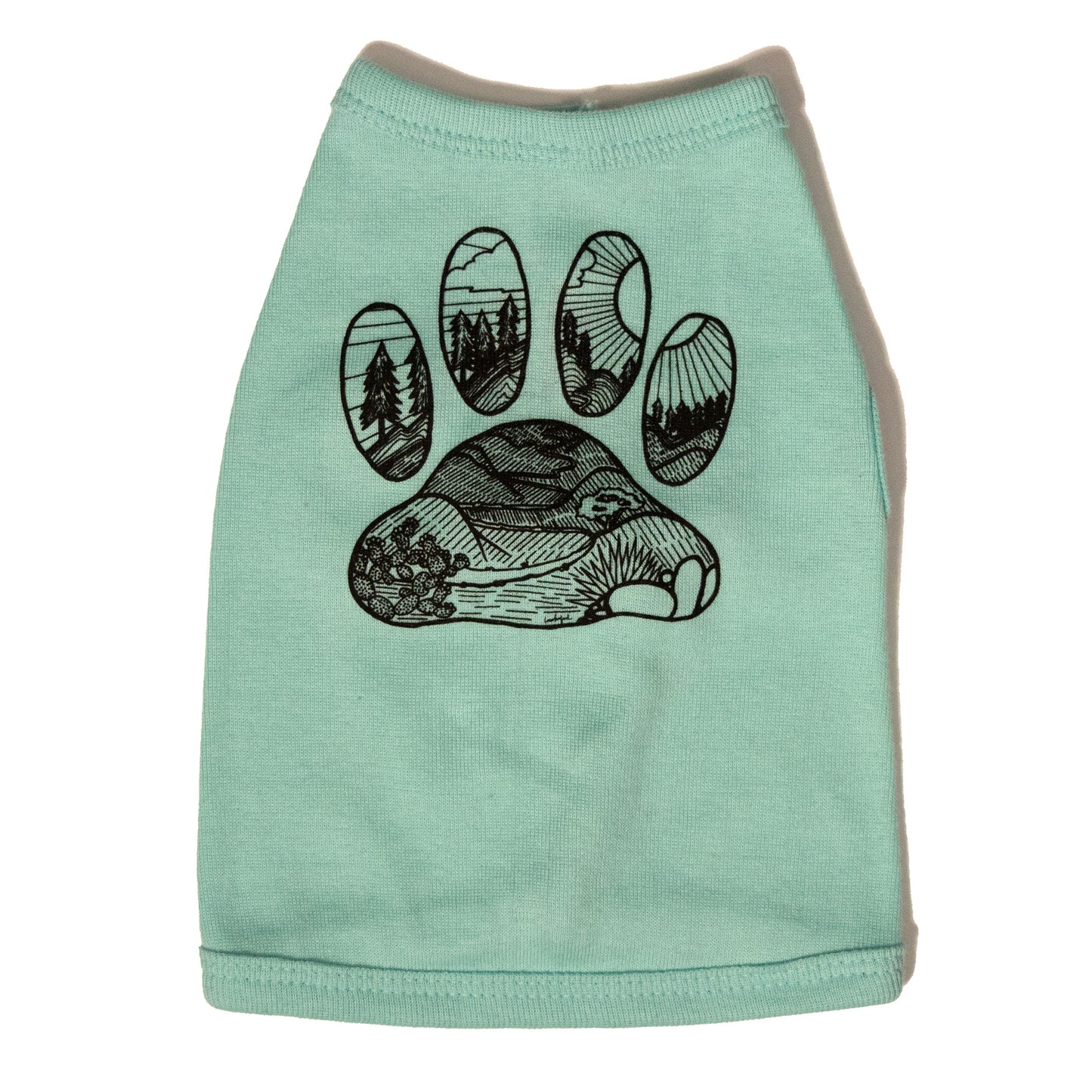A light blue color dog shirt in a tank top style. The illustrated design on the back features a desert floor leading up to mountains with pine trees. The design is inside the shape of a dog paw print. The illustration is in black and the shirt color is light blue.