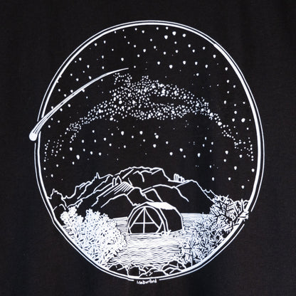 A close up of the design on the t-shirt. A white Desert Camping illustration on the front of the gender neutral black colored t-shirt. The illustration shows a tent in the foreground with mountains in the background, desert plants in the very foreground, and stars, the Milky Way gallaxy, and a shooting star in the sky above the tent. The design is encompassed in a circular shape.