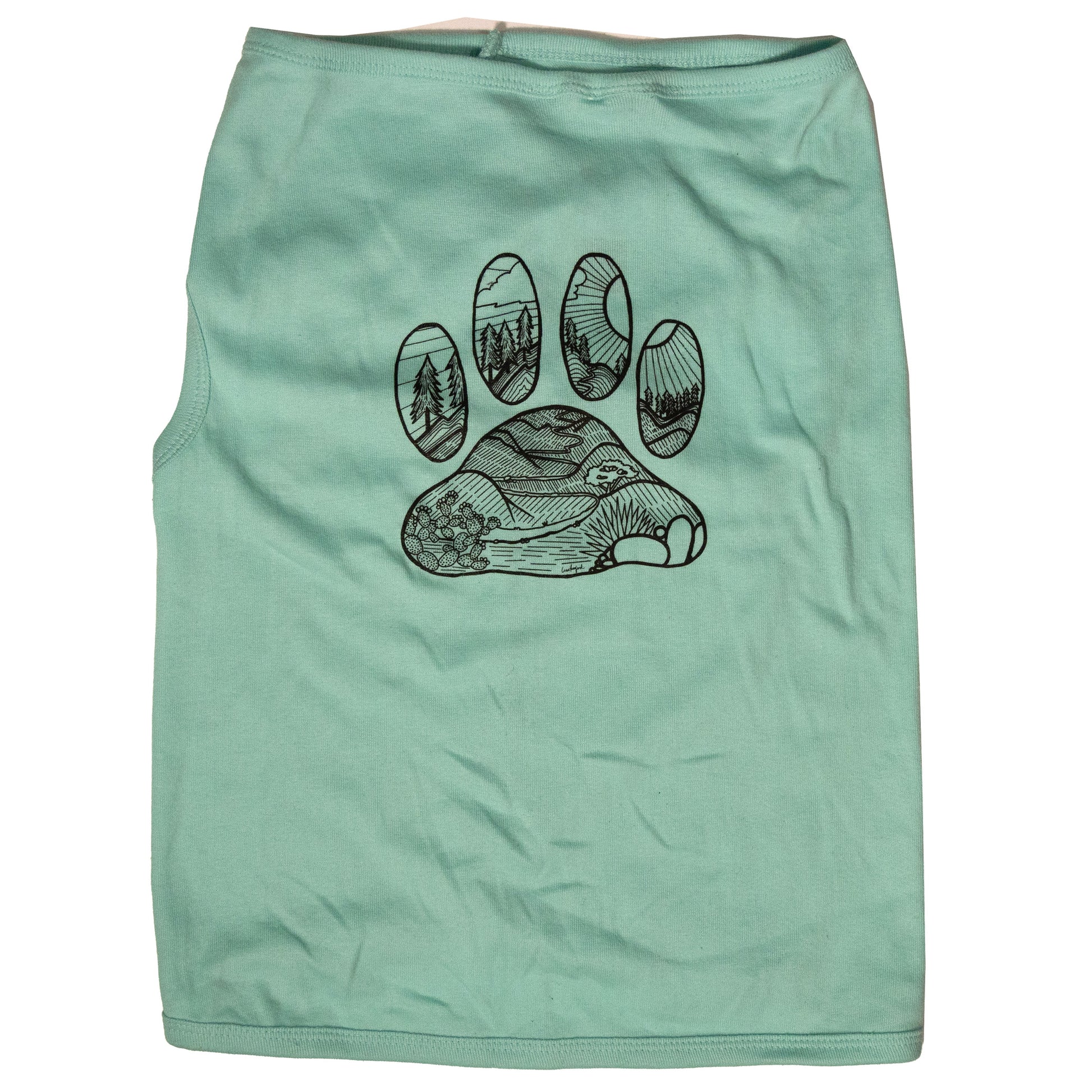 A light blue color dog shirt in a tank top style. The illustrated design on the back features a desert floor leading up to mountains with pine trees. The design is inside the shape of a dog paw print. The illustration is in black and the shirt color is light blue.